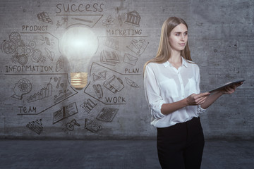 Beautiful business woman against a concrete wall with sketch drawn on it and bright lightbulb