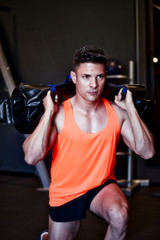 Young muscular athlete performing load exercise with heavy bag, Fitness.