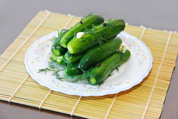 salted green cucumbers with dill and seasoning on a white plate
