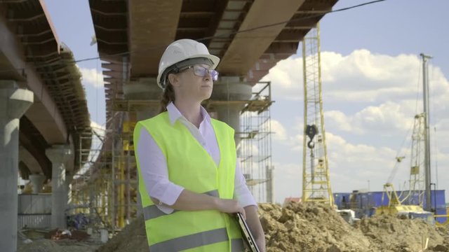 Female builder at construction site of overpass. girl foreman starts to work, opens laptop, inspects construction object.