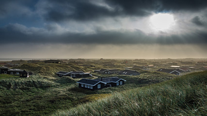 Abendstimmung über einer Ferienhaussiedlung in Dänemark, die Sonne scheint durch dunkle Wolken - obrazy, fototapety, plakaty