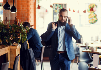 Young bearded businessman walks into a stylish loft office talking on the phone.
