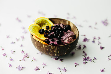 healthy smoothie bowl breakfast in coconut plate with lilac flowers