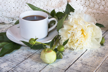 Morning cup of coffee and beautiful white peonies on a white wooden table.