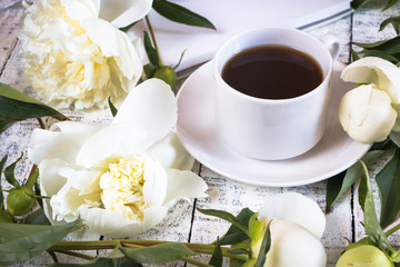Morning cup of coffee and beautiful white peonies on a white wooden table.