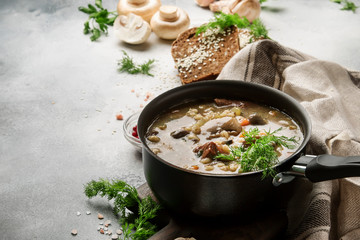 Hot meat vegetable mushroom soup with beef and wholegrain barley. With black bread, in metal pan, top view, gray kitchen table, copy space