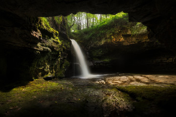 A small cave at the side of Sgwd Ddwli Isaf waterfall in Waterfall Country on the river Neath, near Pontneddfechan in South Wales, UK.