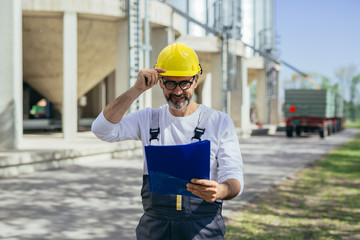 worker reading instructions. grain silos and tractor in blurred background