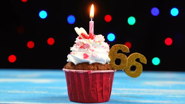 Delicious birthday cupcake with burning candle and number 66 on multicolored blurred lights background