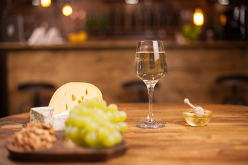 White wine glasss with white grapes and cheese on wooden table