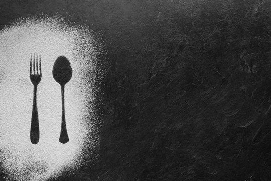 Spoon and fork silhouette made with flour on dark texture background