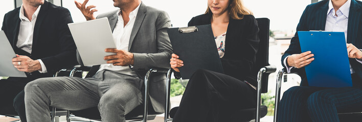 Businesswomen and businessmen holding resume CV folder while waiting on chairs in office for job interview. Corporate business and human resources concept.