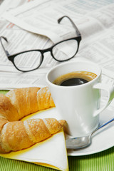 Small quick breakfast with croissant and newspaper, copy space, upright format