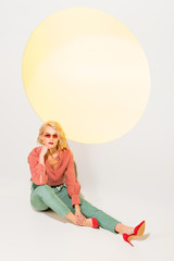 beautiful stylish girl in colorful clothes and sunglasses posing on white with yellow circle