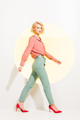 beautiful stylish girl in colorful clothes looking at camera and posing on white with yellow circle