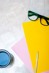 Yellow tulip, coffee, green glasses and colorful paper on marble background