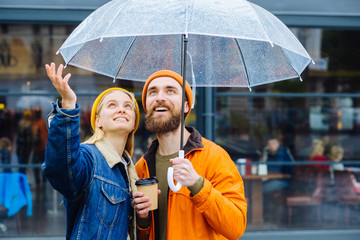 Doesn't stop raining soon concept. Hipster couple under umbrella in rainy spring cold weather urban city street on background. Lifestyle concept.