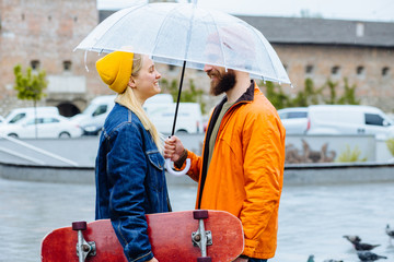 Side view portrait of lovely hipster couple face to face embracing under transparent umbrella...