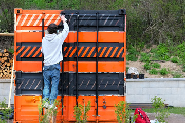 Spray paint an on the iron warehouse trailer. Young repairman is working with paint in spray....