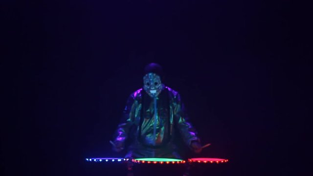 Epic performance of an African drummer in the rays of a laser. The drummer’s performance in a mask expressively beats the drum’s rhythm.