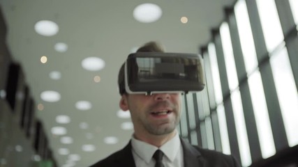 Close-up shot of middle aged businessman in virtual reality headset having video call and talking while walking along office corridor