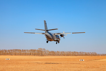 Fototapeta na wymiar A small aircraft for the transport of passengers and paratroopers lands in a field on a landing strip with grass under a blue sky above the trees on a clear cloudless day. Air patrol.