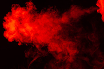 Portrait of a side mouth part of guys face with a colored backlight of monochrome smoking a vape and exhaling white red in different directions on a black isolated background. Puffs harmful to health.