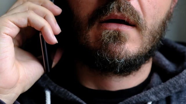 Close up portrait of bearded man talking on smart phone, focus on lips, no eyes, secret talk, criminal threatening someone