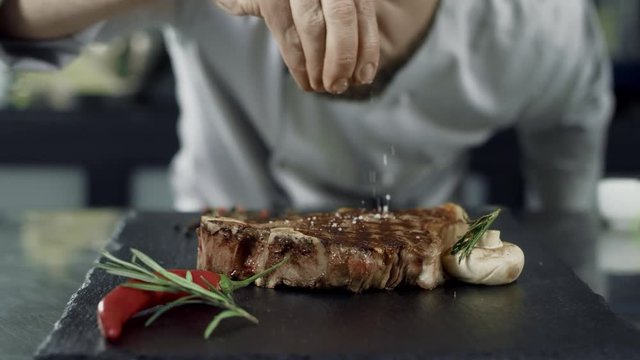 Chef salt frying meat at griddle. Closeup man hands salt steak in slow motion.