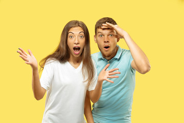 Fototapeta premium Beautiful young couple's half-length portrait on yellow studio background. Woman and man in shirts looking for something and wondering. Facial expression, human emotions concept. Trendy colors.