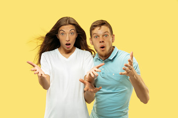 Beautiful young couple's half-length portrait on yellow studio background. Woman and man in shirts asking or shocked of something. Facial expression, human emotions concept. Trendy colors.