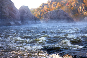 Morning haze over the water of the wild mountain river with rapids. Autumn morning landscape of the river