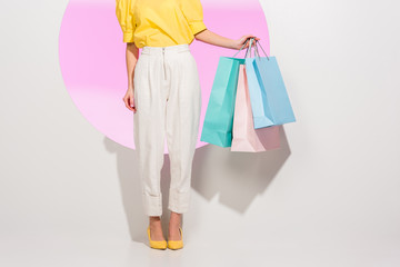 partial view of stylish girl holding colorful shopping bags on white with pink circle