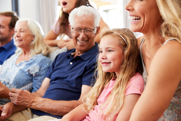 Multi-Generation Family Sitting On Sofa At Home Watching Movie Together