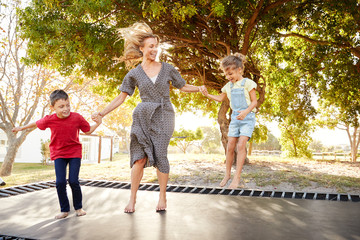 Mother Playing With Children On Outdoor Trampoline In Garden