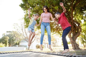 Siblings With Teenage Sister Playing On Outdoor Trampoline In Garden