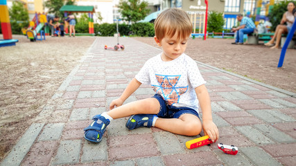 Portrait of little toddler boy playing with toy cars on the playground