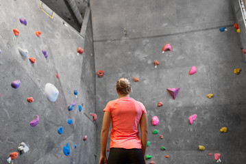 fitness, extreme sport, bouldering, people and healthy lifestyle concept - young woman at indoor climbing wall in gym from back