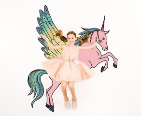 top view of cheerful kid looking at camera and gesturing near unicorn on white © LIGHTFIELD STUDIOS