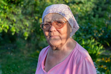Outdoor summer portrait of an eldery seniour woman, close-up, grandmother of 80-90 years old wearing eyeglasses and kerchief