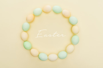 top view of round frame made of painted chicken eggs on light yellow background with Easter lettering