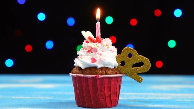 Delicious birthday cupcake with burning candle and number 82 on multicolored blurred lights background