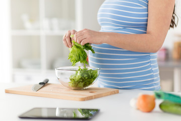 pregnancy, cooking food and healthy eating concept - close up of pregnant woman chopping lettuce by hands for salad at home kitchen