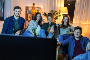 friendship and leisure concept - happy friends with non-alcoholic drinks watching tv at home in evening