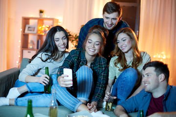 friendship, technology and party concept - happy friends with smartphone and non-alcoholic drinks at home in evening