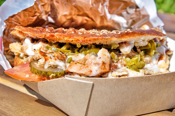 closeup view of chicken doner kebab sandwich in natural light on open air restaurant wooden table against green plant grass background turkish middle east arabian national food concept
