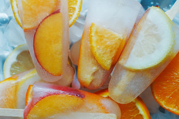 Homemade orange and peach popsicles with ice and citrus slices on light background