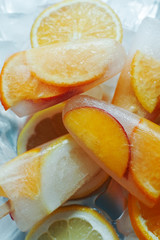 Homemade orange and peach popsicles with ice and citrus slices on light background