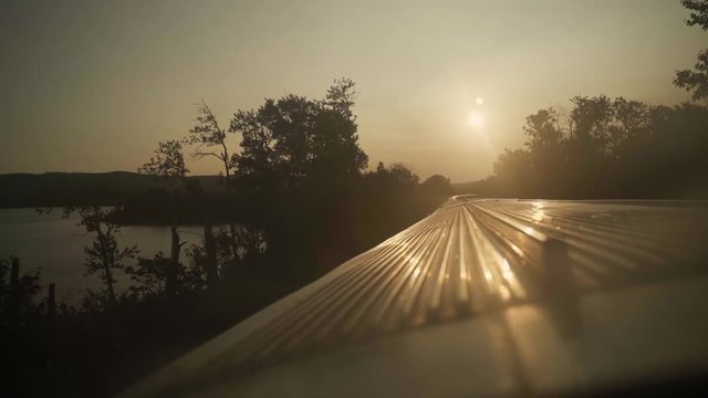 A forest and the roof of a sightseeing train in movement seen trough its window - panoramic view during sunrise - golden hour light.