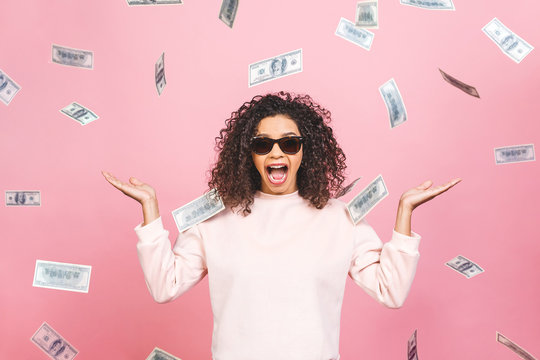 Concept photo of a cheerful afro american woman standing under rain with money isolated against pink background.